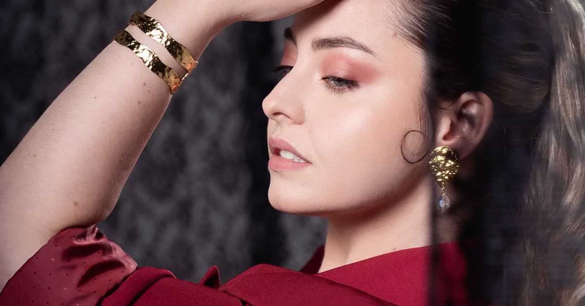 Mujer con maquillaje para invitada de boda, tonos cálidos en los ojos y acabado luminoso en la piel, vestida de rojo y con accesorios dorados elegantes